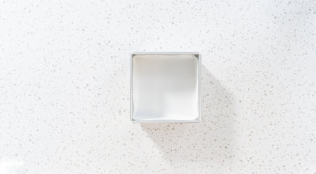 Flat lay. Lining square cheesecake pan with parchment paper sheet to prepare chocolate pistachio fudge.の写真素材