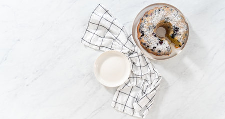 Flat lay. Slicing freshly baked lemon blueberry bundt cake with powdered sugar dusting.の写真素材