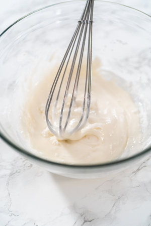 Mixing ingredients with a hand mixer in a large mixing bowl to make the lemon glaze for mini Easter bread kulich.の写真素材