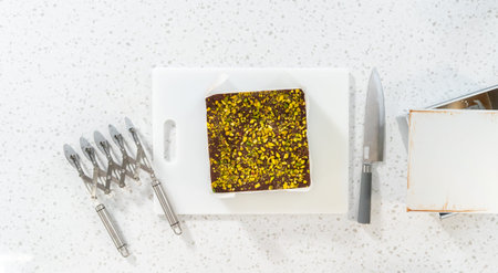 Flat lay. Removing chocolate pistachio fudge from a square cheesecake pan lined with parchment.の写真素材