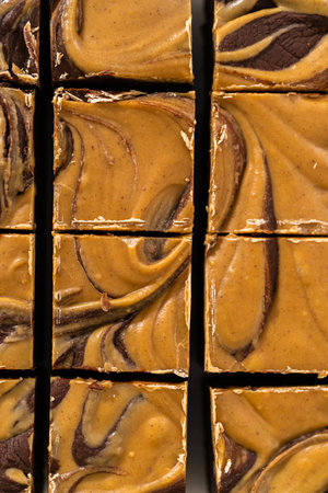 Cutting chocolate fudge with peanut butter swirl into small pieces on a white cutting board.の写真素材