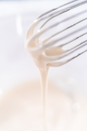 Mixing ingredients in a glass mixing bowl to prepare the white glaze.の写真素材