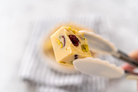 Holding homemade cranberry pistachio fudge square piece with kitchen tongs.の写真素材