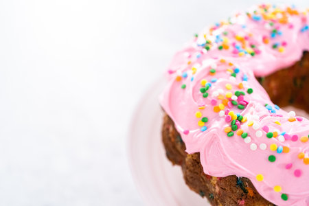 Funfettti bundt cake frosted with pink vanilla buttercream frosting and decorated with rainbow sprinkles.の写真素材