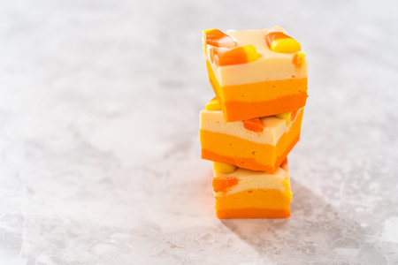 Homemade candy corn fudge square pieces stacked on a kitchen counter.の写真素材