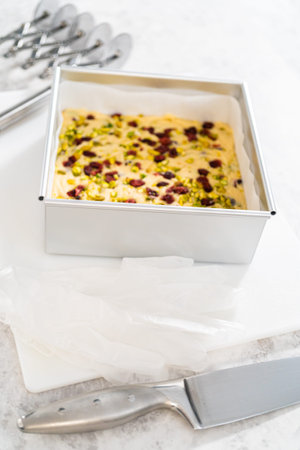 Removing cranberry pistachio fudge from a square cheesecake pan lined with parchment.の写真素材