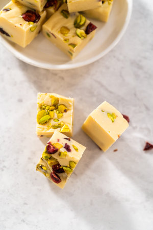 Homemade cranberry pistachio fudge square pieces on a kitchen counter.