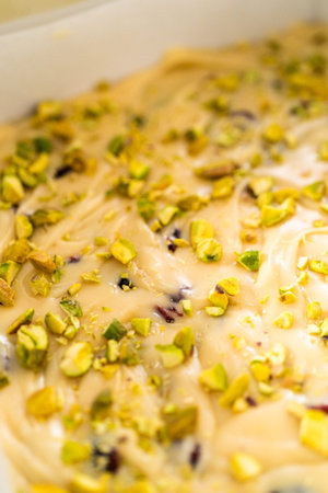 Filling square cheesecake pan lined with parchment paper with fudge mixture to prepare cranberry pistachio fudge.の写真素材