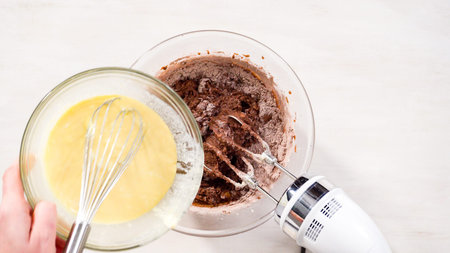 Step by step. Flat lay. Mixing ingredients in a glass mixing bowl to bake chocolate bundt cake with...