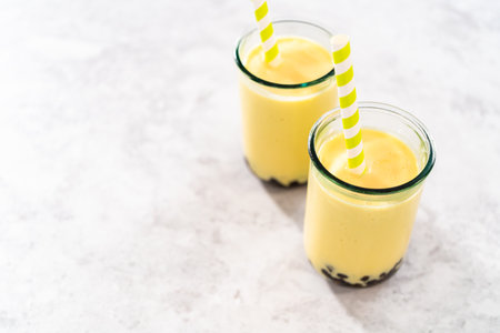 Freshly made mango boba smoothie in a drinking glass with a paper straw.の写真素材