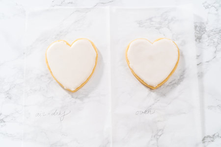 Decorating heart-shaped sugar cookies with pink and white royal icing for Valentines Day.