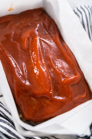 Glazing classic meatloaf with sweet glaze in a loaf pan lined with parchment paper.の写真素材