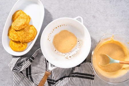 Flat lay. Frying pumpkin pancakes batter on a white frying pan.の写真素材