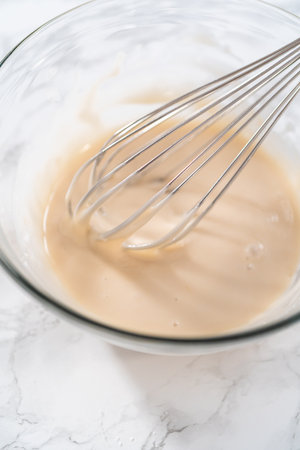 Lemon glaze. Mixing ingredients with a hand whisk in a glass mixing bowl to make lemon glaze.の写真素材