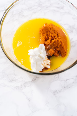 Mixing ingredients in a large glass mixing bowl to bake pumpkin bunt cake.の写真素材