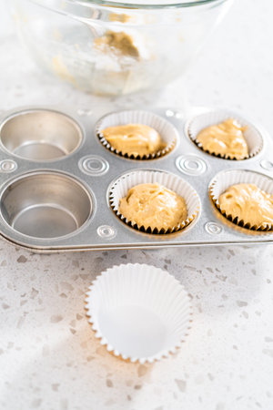 Scooping cupcake batter with dough scoop into a baking cupcake pan with liners to bake dulce de...