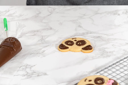 Icing panda-shaped shortbread cookies with chocolate icing.