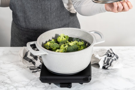 Steaming fresh broccoli in a cooking pot with a steamer basket to prepare steamed broccoli.
