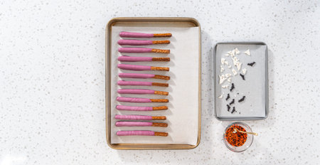 Flat lay. Dipping pretzel rods into melted chocolate to make Halloween chocolate-covered pretzel...