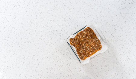 Flat lay. Pouring fudge mixture into the square glass baking pan lined with parchment paper to prepare pumpkin spice fudge.の写真素材