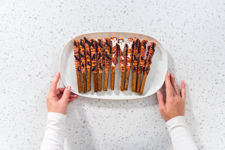 Flat lay. Halloween chocolate-covered pretzel rods with sprinkles on a white serving plate.の写真素材