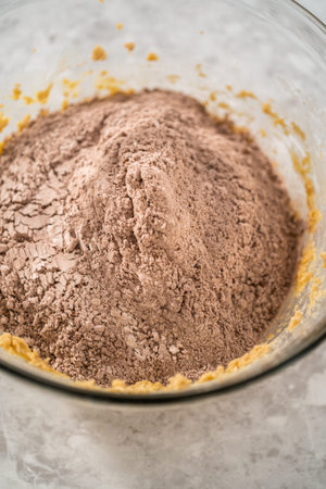 Mixing ingredients in a large glass mixing bowl with a kitchen mixer to bake chocolate cookies with...