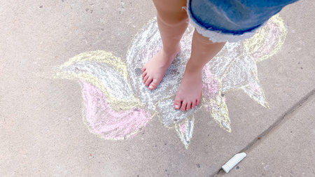 Little girl drawing chalk art on a suburban driveway on a summer day.