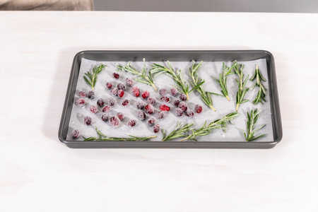 Covering fresh cranberries and rosemary in sugar to decorate chocolate bundt cake with chocolate...