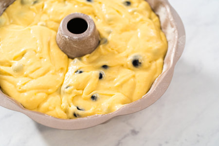Filling metal bundt cake pan with cake butter to bake lemon blueberry bundt cake.の写真素材