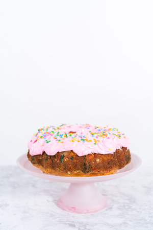 Funfettti bundt cake frosted with pink vanilla buttercream frosting and decorated with rainbow...