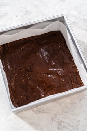 Filling square cheesecake pan lined with parchment paper with fudge mixture to prepare candy cane...