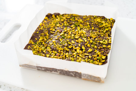 Removing chocolate pistachio fudge from a square cheesecake pan lined with parchment.の写真素材