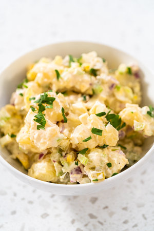Serving potato salad garnished with fresh parsley in a white ceramic bowl.の写真素材