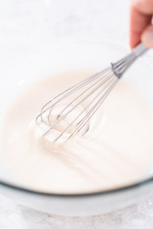 Mixing ingredients in a glass mixing bowl to prepare the white glaze.の写真素材