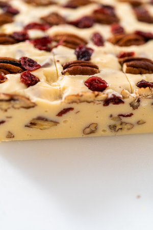 Cutting white chocolate cranberry pecan fudge into small pieces on a white cutting board.の写真素材