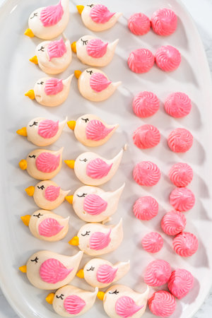 Decorating mini Easter bread kulich with sprinkles and meringue bird-shaped cookies.の写真素材