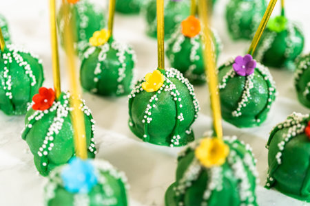 Cactus-shaped cake pops, beautifully decorated with luster dust, sugar flowers, and white sprinkles,...