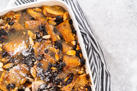 Serving freshly baked bread pudding with raising and almond slivers in a white casserole dish.の写真素材