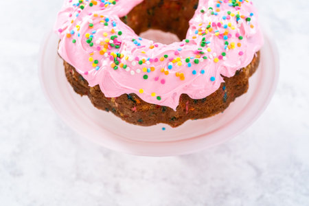 Funfettti bundt cake frosted with pink vanilla buttercream frosting and decorated with rainbow...