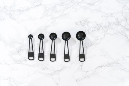 Flat lay. Black metal measuring spoons for baking on a marble countertop.の写真素材