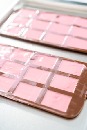 Filling silicone chocolate mold with melted chocolate to make mini pink chocolates.