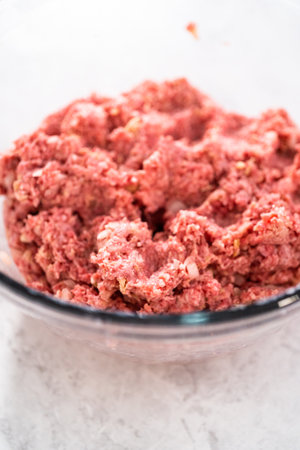 Mixing ingredients with hands in a glass mixing bowl to make meatloaf.の写真素材