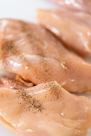 Shredded chicken in a pressure cooker. Seasoning chicken breasts with salt and ground pepper on a white cutting board.の写真素材