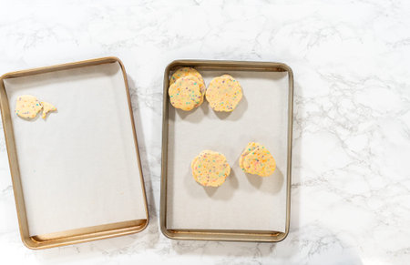 Flat lay. Large quantity of sprinkle-filled sugar cookies are neatly stacked on a baking tray,...