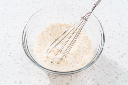 Mixing dry ingredients with a hand whisk in a large glass mixing bowl to bake cupcakes.の写真素材