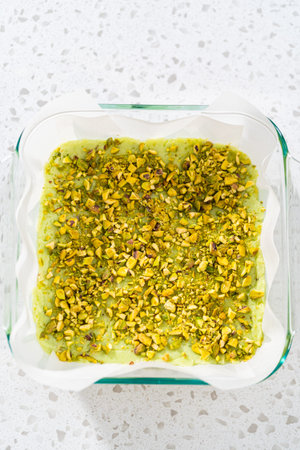Pouring fudge mixture into the square glass baking pan lined with parchment paper to prepare pistachio fudge.の写真素材