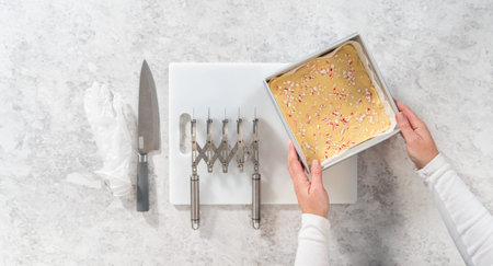 Flat lay. Removing candy cane fudge from a square cheesecake pan lined with parchment.の写真素材