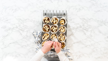 Flat lay. Garnishing no-yeast cinnamon roll cupcakes with cream cheese frosting from the piping bag.