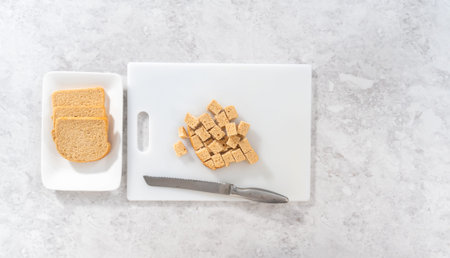 Flat lay. Cutting stale bread with a bread knife on a white cutting board to make croutons.の写真素材