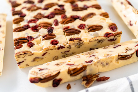 Cutting white chocolate cranberry pecan fudge into small pieces on a white cutting board.の写真素材